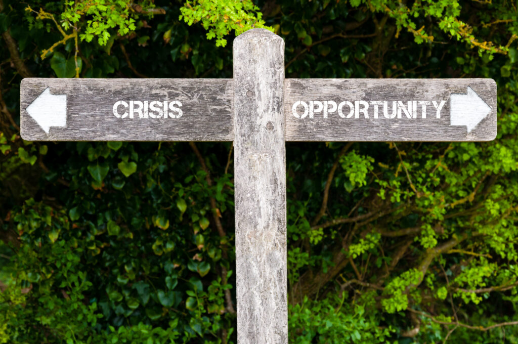 Wooden signpost with two opposite arrows over green leaves background. CRISIS versus OPPORTUNITY directional signs, Choice concept image